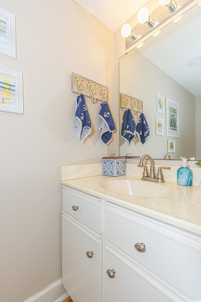 bathroom featuring baseboards, visible vents, a textured ceiling, and vanity