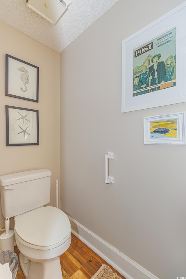 bathroom with toilet, a textured ceiling, baseboards, and wood finished floors