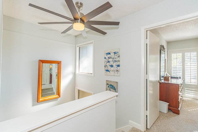 hallway featuring a textured ceiling, carpet floors, and an upstairs landing