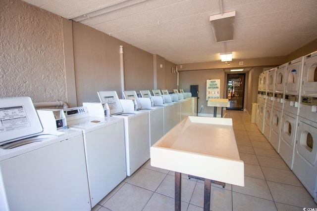 community laundry room with stacked washer / dryer, light tile patterned flooring, a textured wall, and washer and clothes dryer