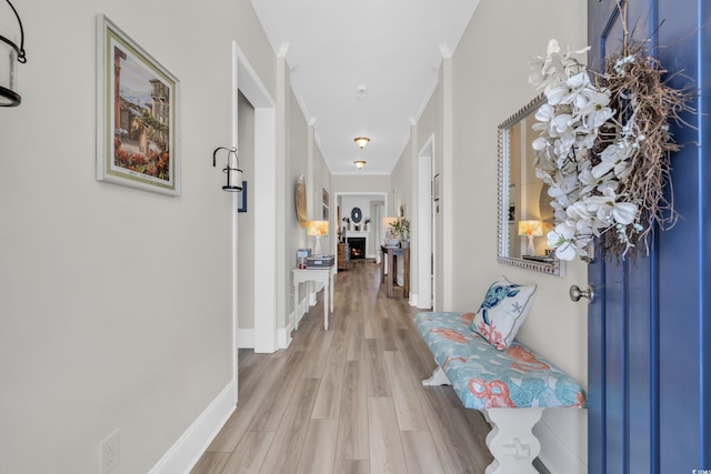 corridor featuring ornamental molding, baseboards, and light wood finished floors