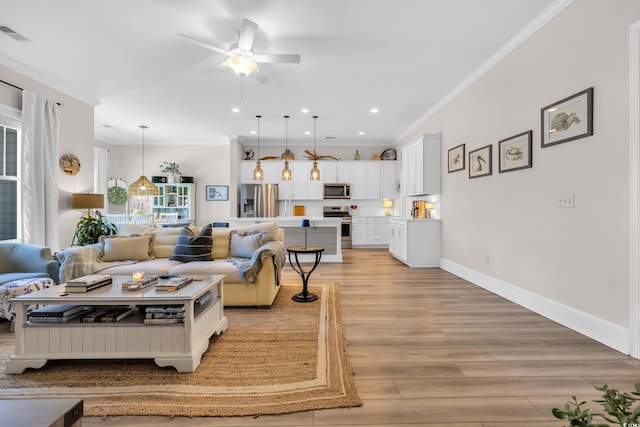 living area with crown molding, recessed lighting, light wood-style flooring, ceiling fan, and baseboards