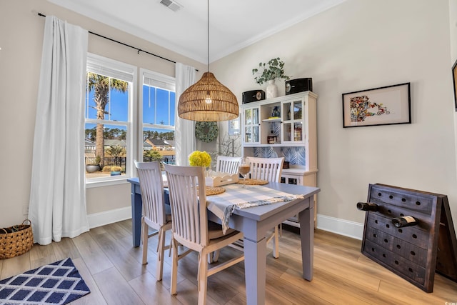 dining area with ornamental molding, light wood-type flooring, visible vents, and baseboards