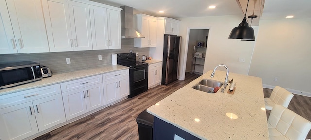 kitchen with a sink, wall chimney range hood, dark wood-style floors, black appliances, and tasteful backsplash