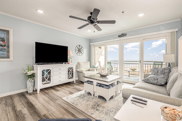 living room featuring a textured ceiling, ornamental molding, wood finished floors, and baseboards