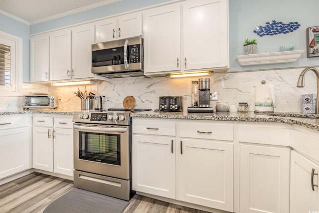 kitchen with light wood finished floors, appliances with stainless steel finishes, ornamental molding, light stone countertops, and white cabinetry