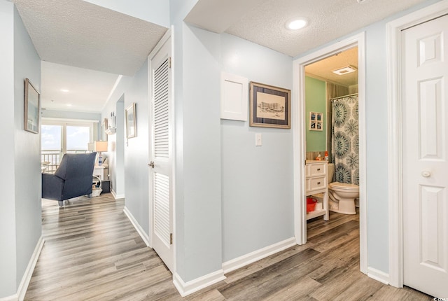 corridor with visible vents, baseboards, a textured ceiling, and light wood finished floors