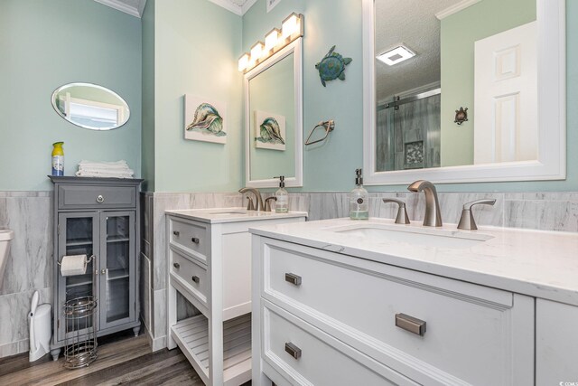 full bath with a wainscoted wall, two vanities, a sink, a shower stall, and a textured ceiling