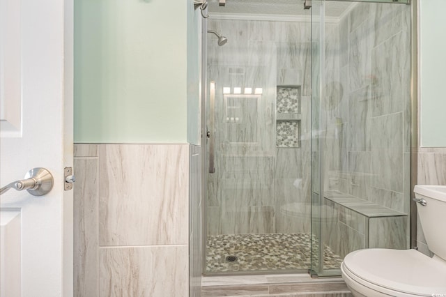 bathroom with a wainscoted wall, a stall shower, toilet, and tile walls