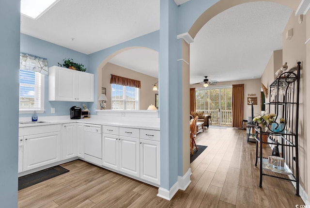 kitchen featuring white dishwasher, a sink, white cabinetry, light countertops, and light wood-type flooring