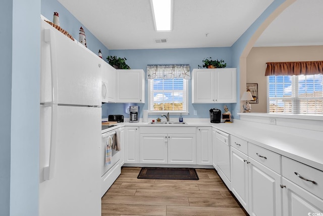 kitchen with white appliances, visible vents, white cabinets, light wood-type flooring, and a sink