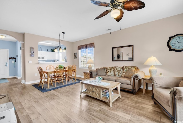 living area featuring arched walkways, light wood-style flooring, baseboards, and ceiling fan with notable chandelier