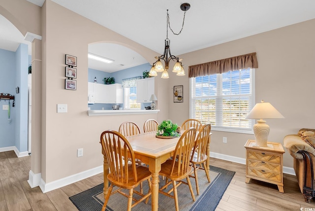 dining space with light wood-style floors, baseboards, arched walkways, and an inviting chandelier