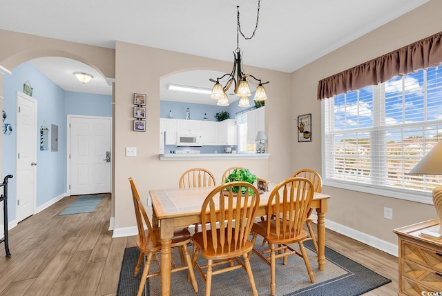 dining space featuring arched walkways, light wood-type flooring, and baseboards