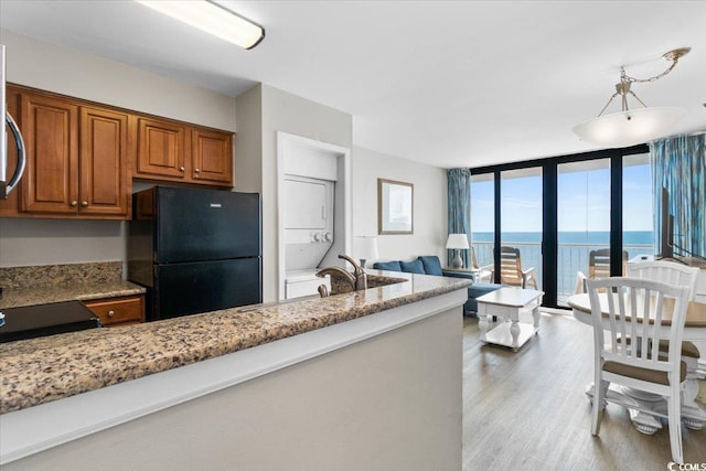 kitchen with light wood-style flooring, brown cabinets, freestanding refrigerator, light stone countertops, and floor to ceiling windows