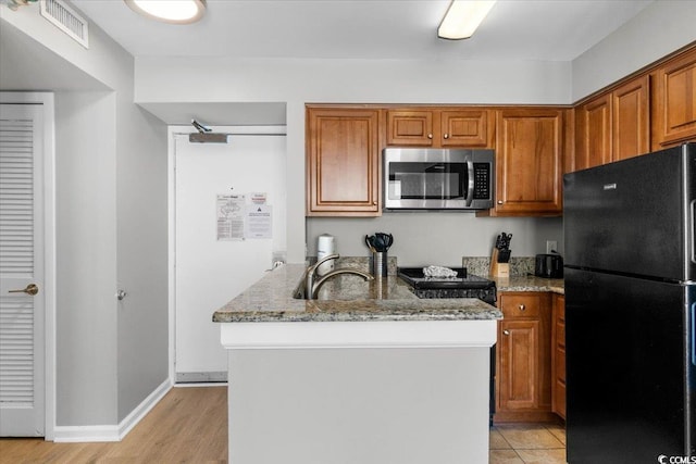 kitchen featuring a peninsula, stove, visible vents, freestanding refrigerator, and stainless steel microwave