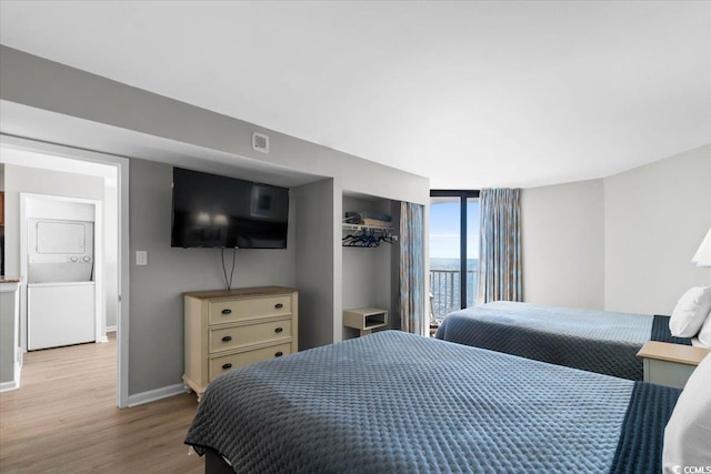 bedroom featuring baseboards, wood finished floors, and stacked washer / drying machine