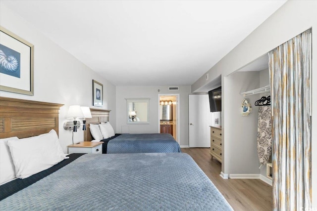 bedroom featuring ensuite bath, baseboards, visible vents, and wood finished floors