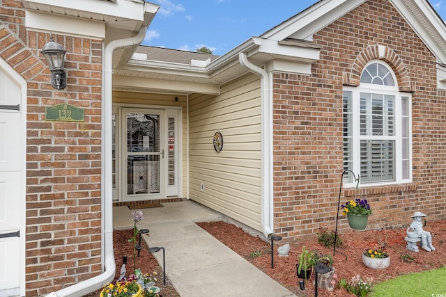 view of exterior entry featuring a garage and brick siding