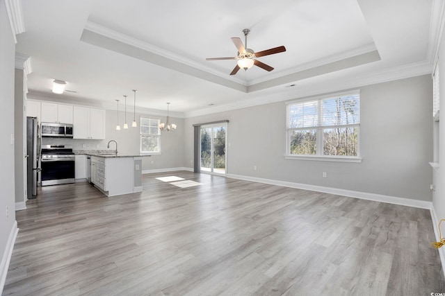 unfurnished living room with light wood-type flooring, baseboards, a raised ceiling, and crown molding