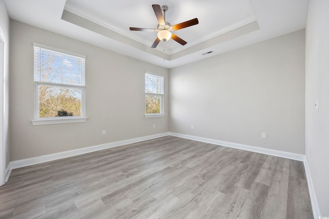 empty room with ornamental molding, a tray ceiling, light wood-style flooring, and baseboards