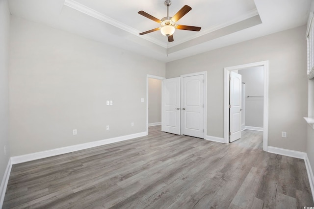 unfurnished bedroom with light wood-type flooring, a tray ceiling, crown molding, and baseboards