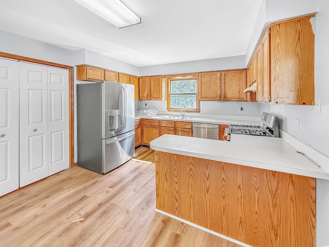 kitchen featuring light wood finished floors, stainless steel appliances, light countertops, under cabinet range hood, and a sink