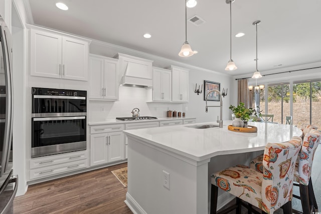 kitchen with visible vents, crown molding, custom range hood, wood finished floors, and stainless steel appliances