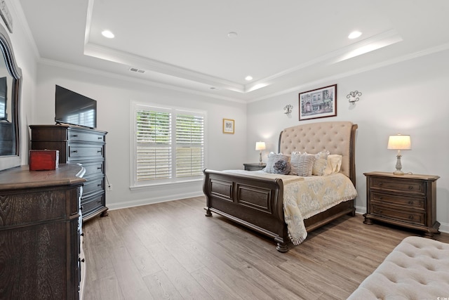 bedroom with a tray ceiling, visible vents, wood finished floors, and ornamental molding