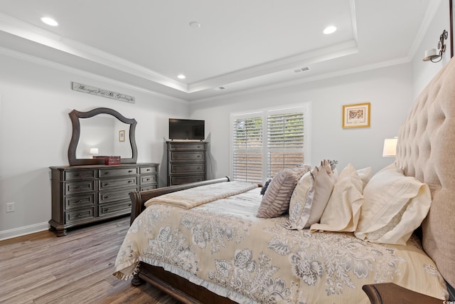 bedroom featuring a raised ceiling, wood finished floors, visible vents, and ornamental molding