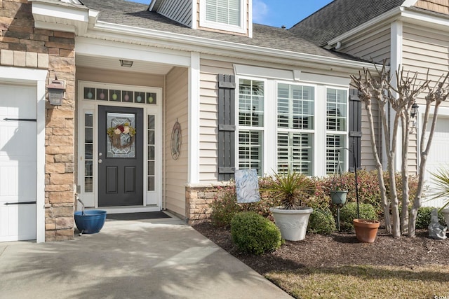 view of exterior entry featuring a garage, stone siding, and roof with shingles