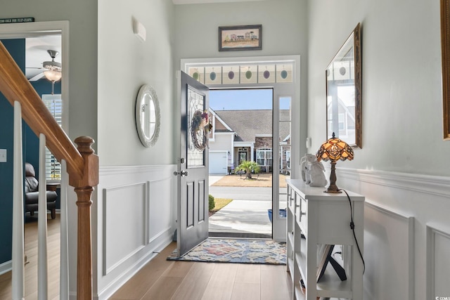 foyer entrance featuring wainscoting, a decorative wall, stairway, and wood finished floors