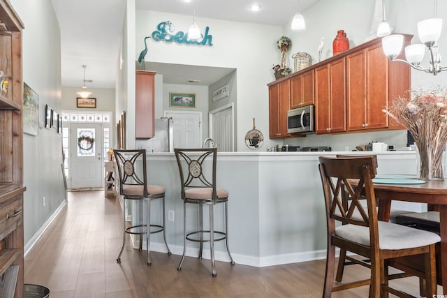 kitchen with a breakfast bar, stainless steel microwave, wood finished floors, and brown cabinets