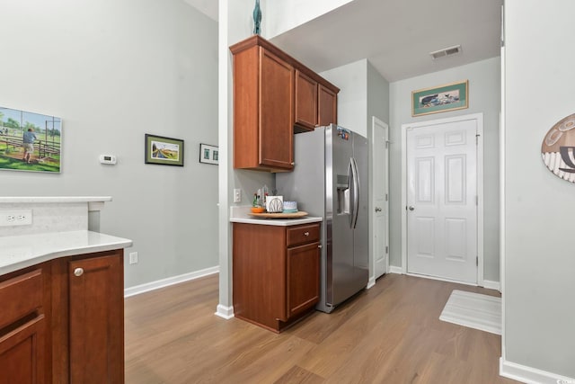 kitchen featuring light countertops, stainless steel refrigerator with ice dispenser, wood finished floors, and visible vents