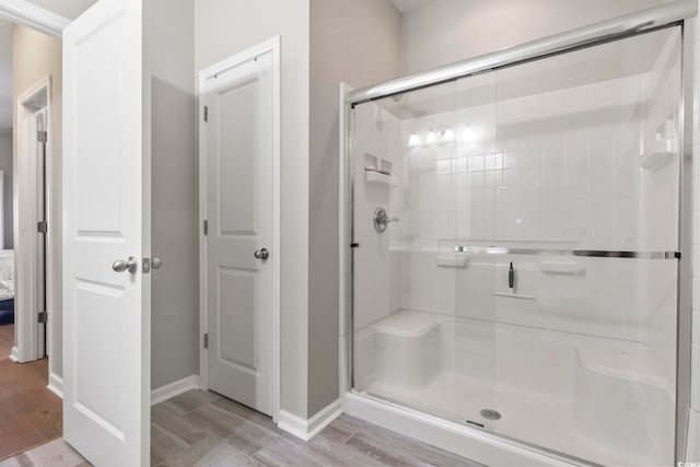 ensuite bathroom with ensuite bath, a shower stall, baseboards, and wood finished floors