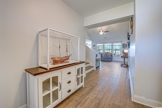 corridor with lofted ceiling, light wood finished floors, stairs, and baseboards