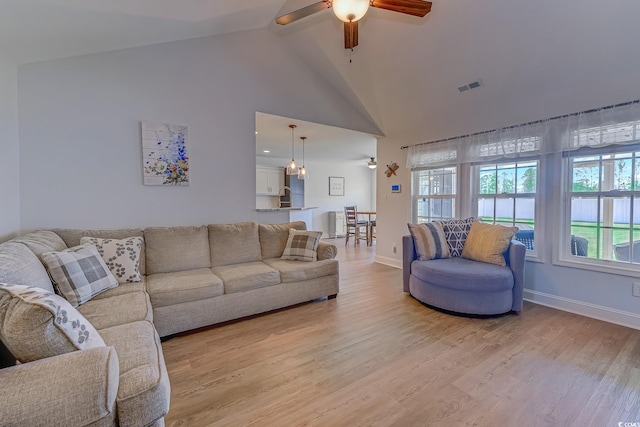 living area with visible vents, light wood-style floors, ceiling fan, high vaulted ceiling, and baseboards