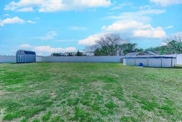 view of yard with a covered pool, a storage unit, a fenced backyard, and an outbuilding