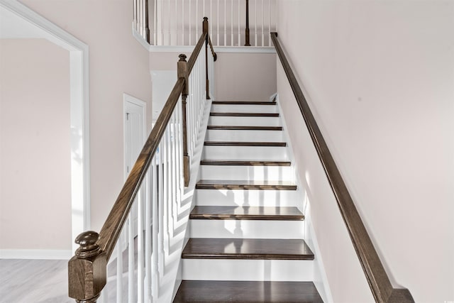 staircase featuring a high ceiling, baseboards, and wood finished floors