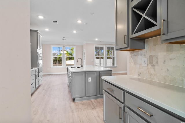 kitchen with a sink, visible vents, light countertops, gray cabinets, and tasteful backsplash