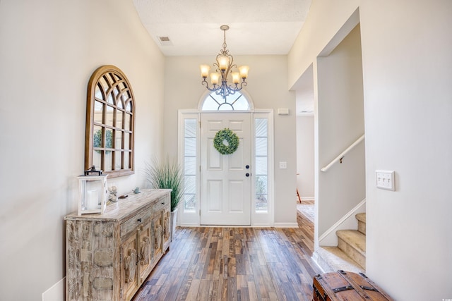 foyer entrance with a chandelier, dark wood-style flooring, visible vents, baseboards, and stairway