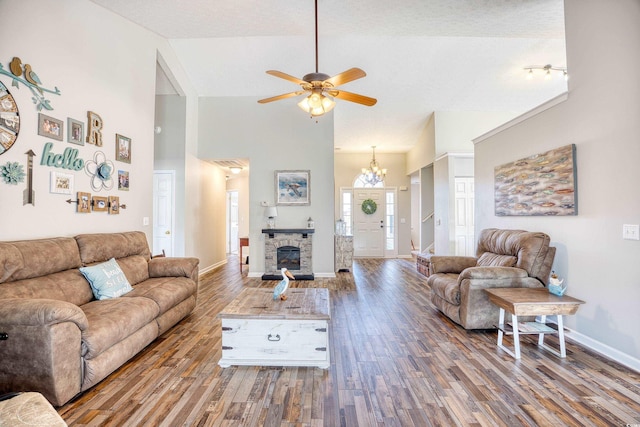 living room featuring high vaulted ceiling, baseboards, wood finished floors, and a stone fireplace