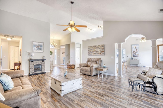 living area featuring arched walkways, a fireplace, decorative columns, wood finished floors, and ceiling fan with notable chandelier