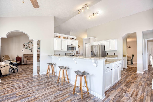 kitchen with arched walkways, stainless steel appliances, white cabinetry, a peninsula, and a kitchen bar