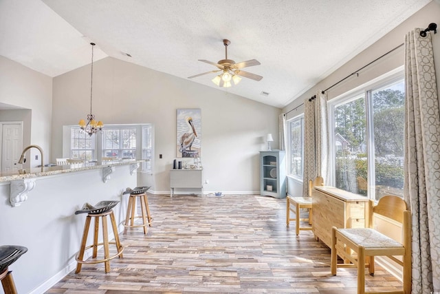 sitting room featuring lofted ceiling, light wood finished floors, a textured ceiling, and ceiling fan with notable chandelier