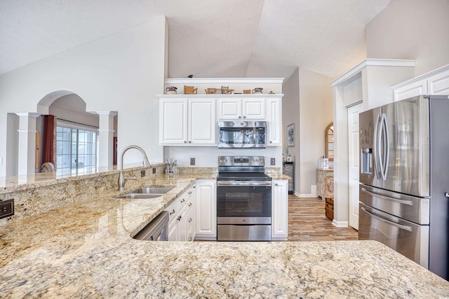 kitchen featuring lofted ceiling, appliances with stainless steel finishes, white cabinetry, a sink, and light stone countertops