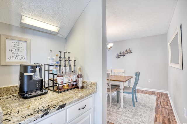 kitchen featuring baseboards, wood finished floors, light stone countertops, a textured ceiling, and white cabinetry