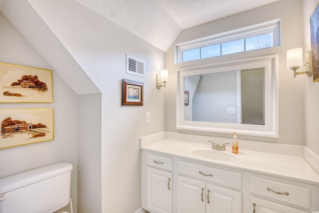 bathroom with visible vents, toilet, vaulted ceiling, a textured ceiling, and vanity