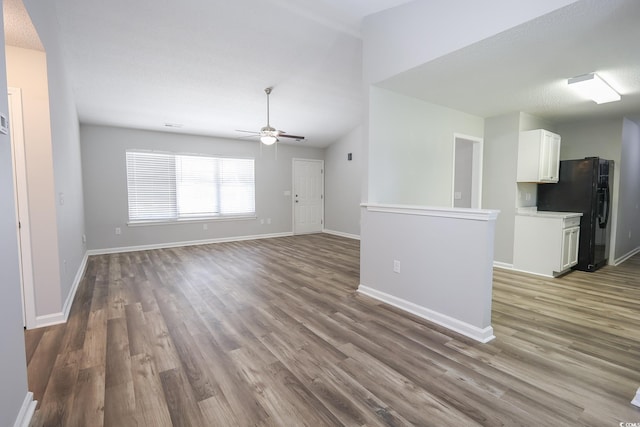 unfurnished living room with a textured ceiling, lofted ceiling, wood finished floors, a ceiling fan, and baseboards