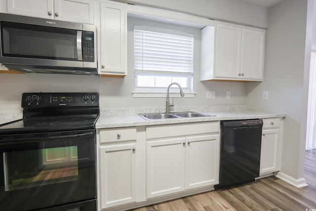 kitchen featuring light wood-type flooring, white cabinets, a sink, and black appliances